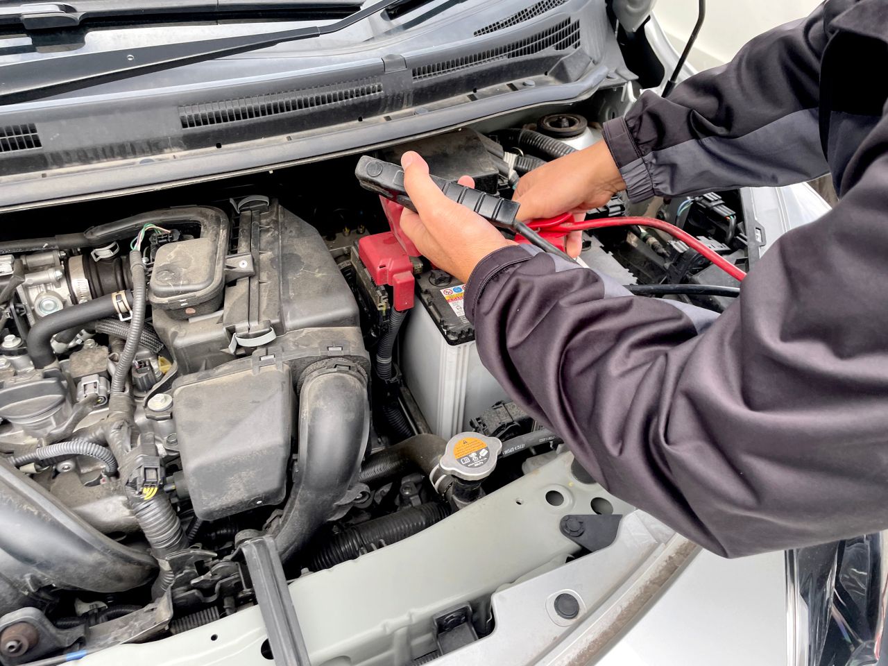 整備士が車のエンジンルーム内で、バッテリーの端子に赤いブースターケーブルのクリップを接続している様子